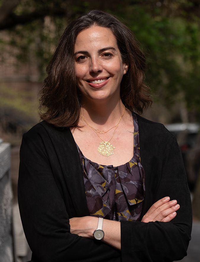 Katina L. Rogers, a woman with fair skin and brown wavy hair, smiling outdoors